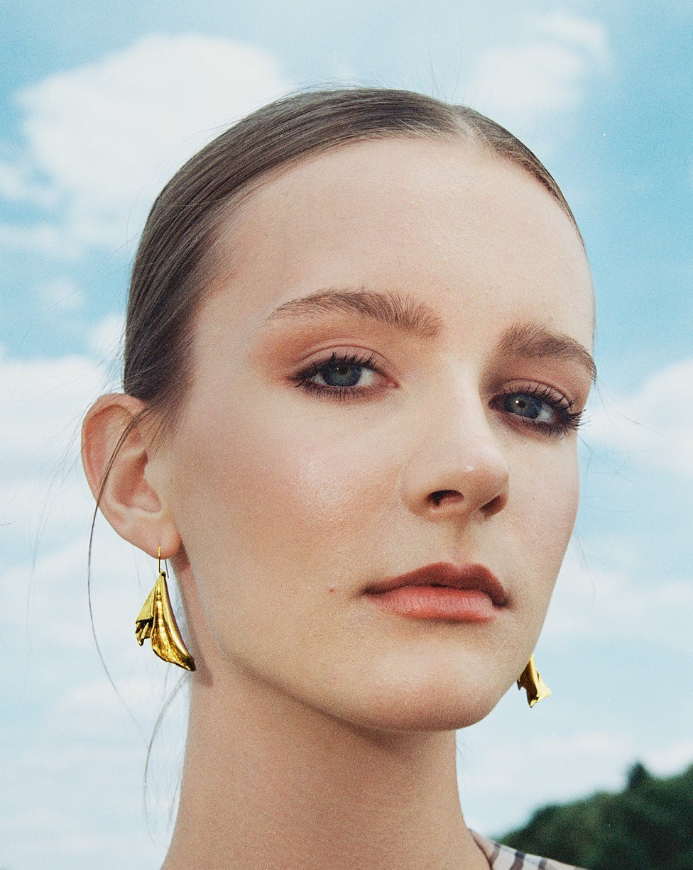Close up of an elegant woman wearing unique gold statement earrings.